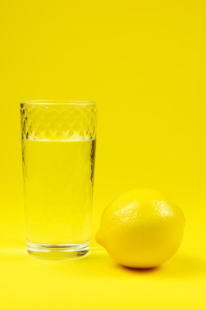 L'eau dans le verre et le citron sur fond jaune vertical