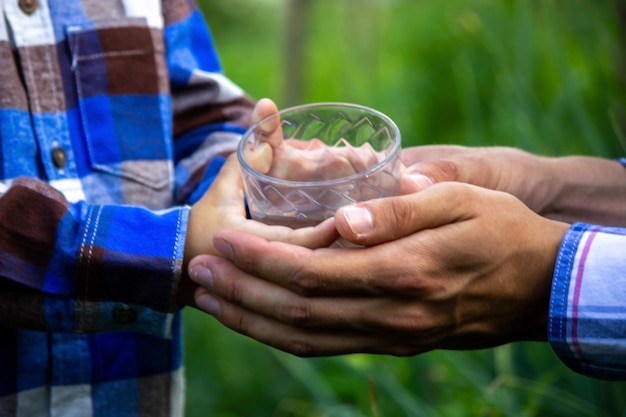 De L'eau Dans Un Verre Entre Les Mains D'un Enfant Et D'un Père. La Nature. Mise Au Point Sélective