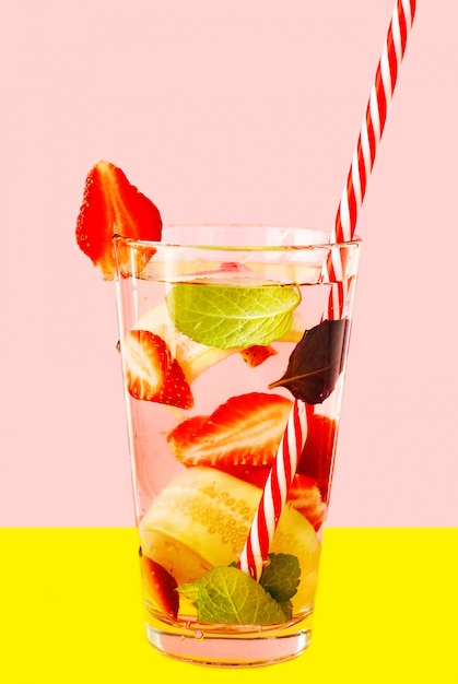 Eau de désintoxication aux fraises et concombre en verre sur le fond rose et jaune.