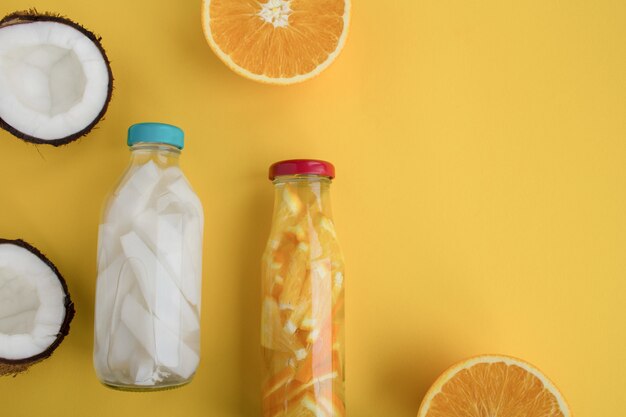 Eau de désintoxication à la noix de coco et à l'orange dans les bouteilles en verre sur fond jaune. Vue de dessus. Espace de copie.