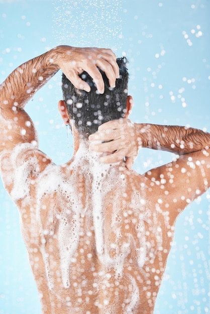 Eau de douche et homme nettoyant le corps avec de la mousse de savon et des produits capillaires sur fond bleu en studio Hygiène de la salle de bain toilettage et dos du corps de lavage masculin pour les soins personnels spa bien-être et soins de la peau