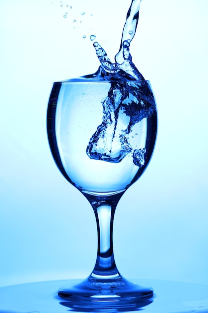 L'eau éclabousse dans un verre. Verser de l'eau dans le verre sur fond bleu