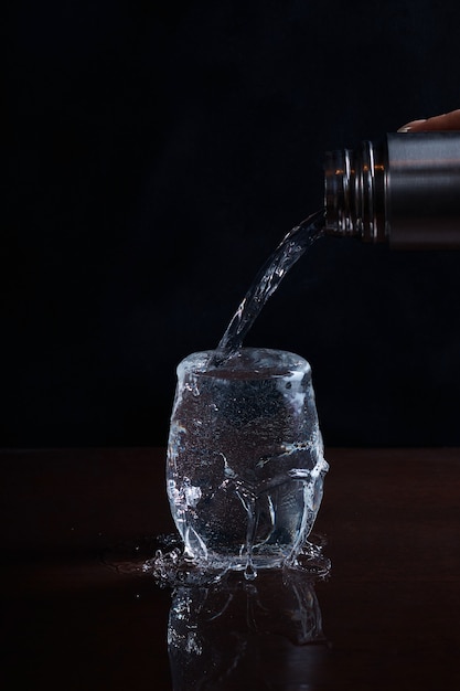 L'eau est versée d'une bouteille dans un verre et déborde sur le bord, surface floue