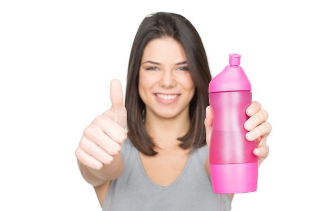 L'eau est la vie. Jeune femme souriante tenant une bouteille de sport et montrant les pouces vers le haut de mise au point sélective