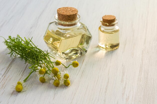 Eau de fleur de camomille ou huile dans une bouteille en verre sur fond de table en bois