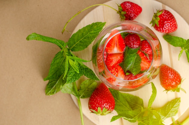 L'eau fraise rafraîchissante ou la limonade décorée à la menthe laisse sur une planche en bois avec espace de copie