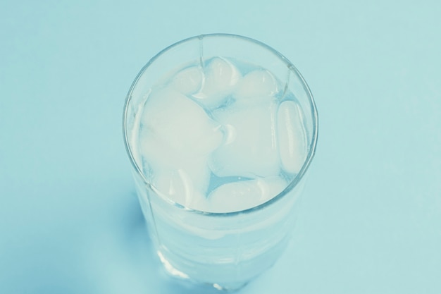 Eau froide rafraîchissante avec de la glace dans un verre sur une surface bleue.