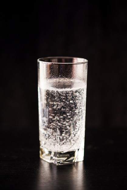 Eau gazée dans un verre sur un tableau noir et fond noir.