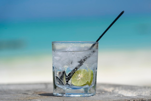 Eau gazeuse avec chaux et glace sur une table en bois près de la mer sur la plage