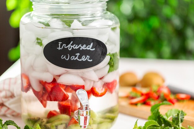 Eau infusée avec des fraises biologiques, du kiwi et de la menthe fraîche dans un distributeur de boissons en verre.