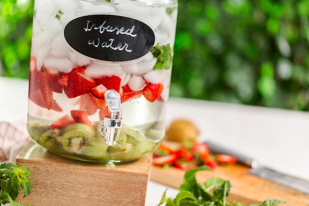 Eau infusée avec des fraises biologiques, du kiwi et de la menthe fraîche dans un distributeur de boissons en verre.