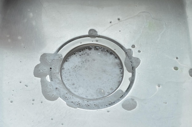 L'eau avec de la mousse de savon dans l'évier en acier s'écoule