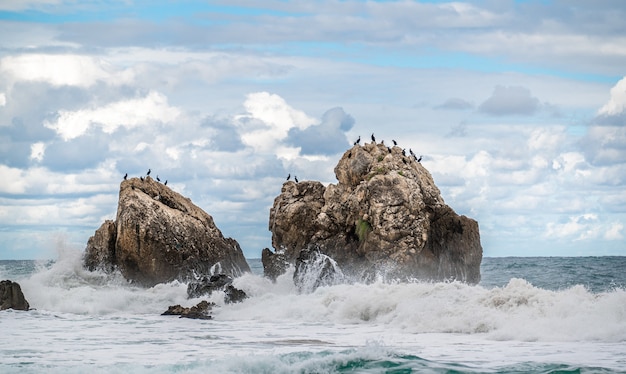 L'eau de l'océan éclabousse sur la plage de rochers avec un beau ciel et des nuages. Vague de mer éclaboussant sur la pierre au bord de la mer en hiver. côte rocheuse avec de l'eau vive tourbillonnant autour des rochers