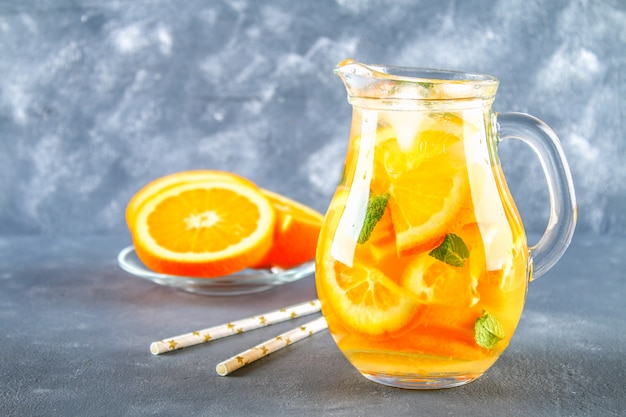 Eau orange de désintoxication dans un pichet sur un fond de béton gris. Alimentation saine, boissons.