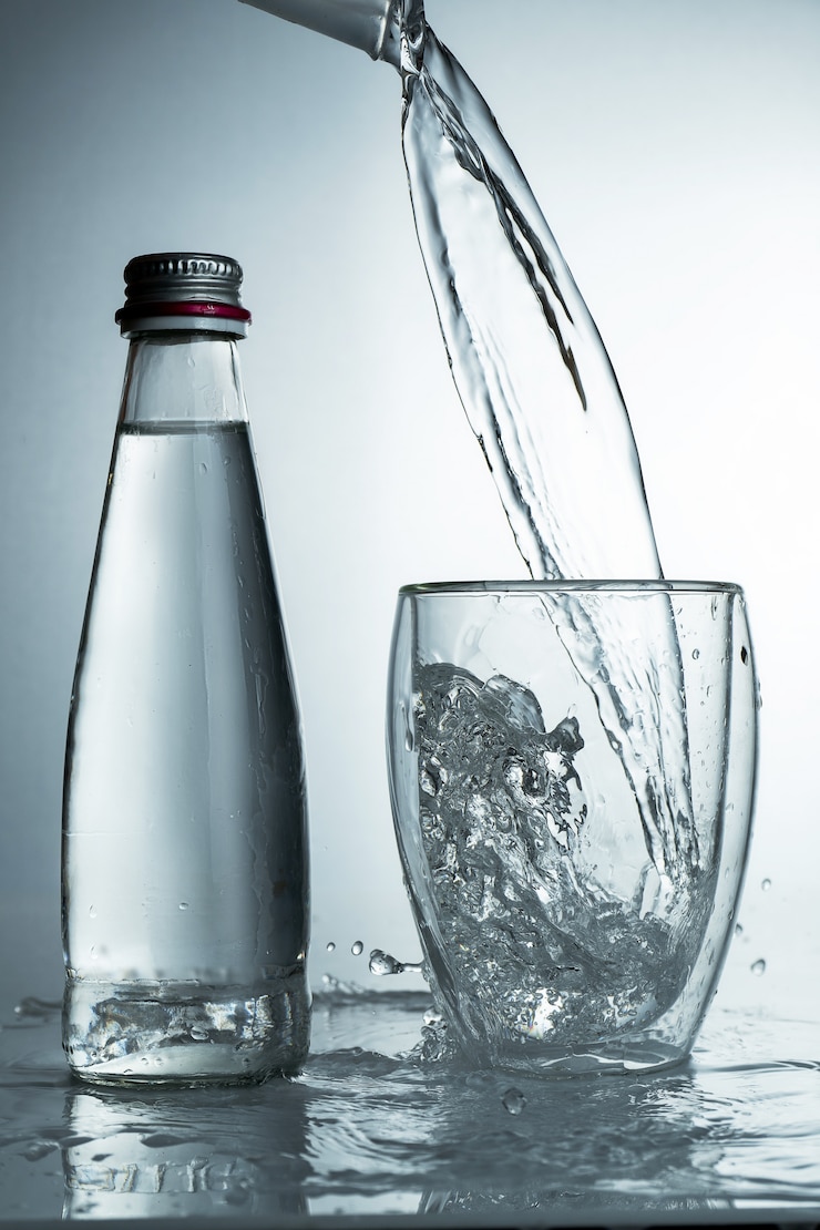 Photo l'eau pure et fraîche et froide est versée dans un verre avec une bouteille. eau purifiée dans un verre sur un mur gris. motion geler les éclaboussures d'eau cristalline sur le mur gris.
