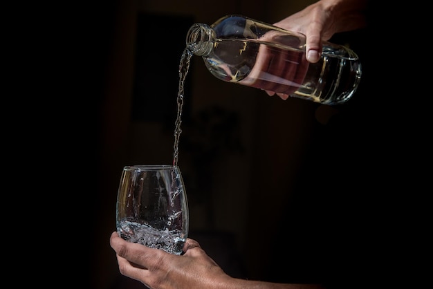 Eau pure tombant dans un gobelet et une bouteille en verre sur fond noir