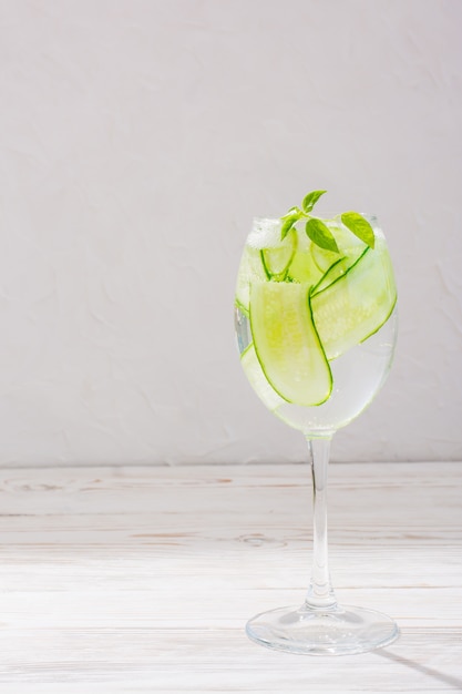 Eau rafraîchissante avec des tranches de concombre et de feuilles de basilic dans un verre sur une table