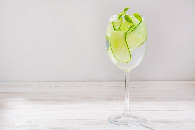 Eau rafraîchissante avec des tranches de concombre et de feuilles de basilic dans un verre