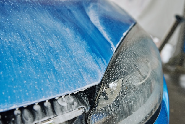 L'eau savonneuse de lavage de voiture s'écoule d'une voiture de nettoyage de voiture bleue lavée avec un lavage haute pression sans contact