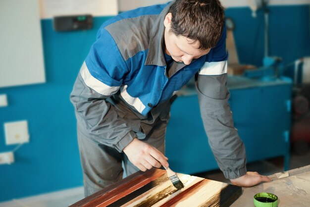 Photo un ébéniste de travail tient un pinceau dans sa main et peint une surface en bois une trace de peinture sur une planche de bois