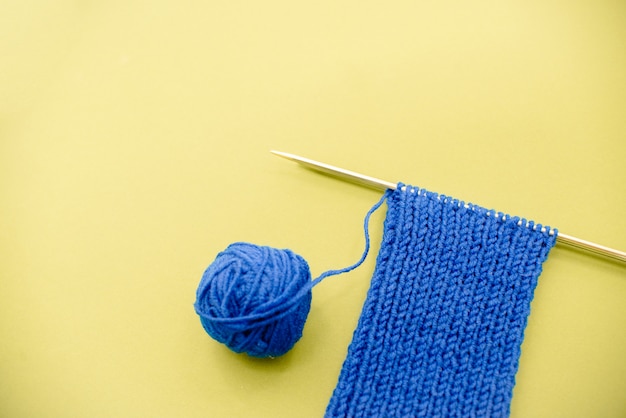 Echarpe tricotée bleu vif avec aiguilles à tricoter fond jaune clair