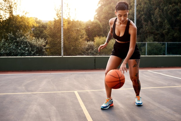 L'échauffement est essentiel Photo pleine longueur d'une jolie jeune sportive debout seule sur un terrain de basket et s'échauffant avec le ballon