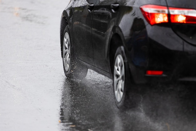 Les éclaboussures d'eau de pluie s'écoulent des roues d'une voiture noire se déplaçant rapidement dans la ville à la lumière du jour avec mise au point sélective