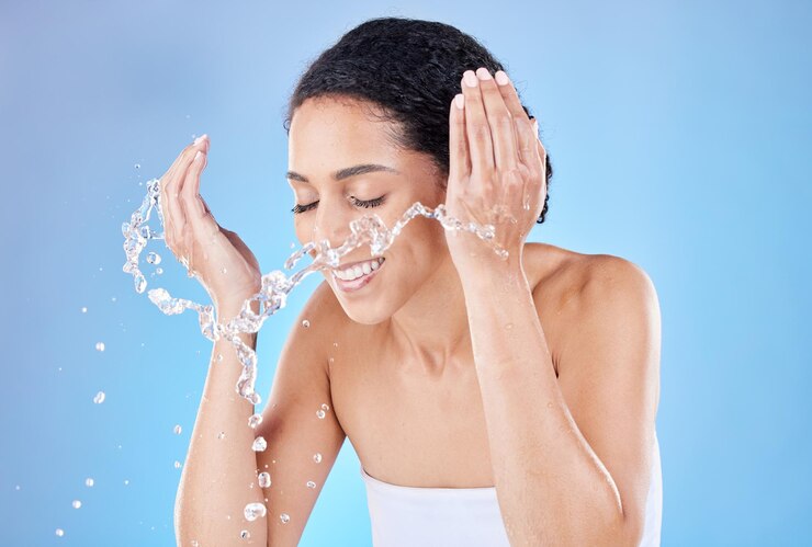 Photo éclaboussures d'eau et soins de la peau femme en studio pour le nettoyage du visage, bien-être du matin et éclat sain avec un fond bleu pour l'espace publicitaire modèle de beauté avec de l'eau dans les mains pour le lavage cosmétique du visage