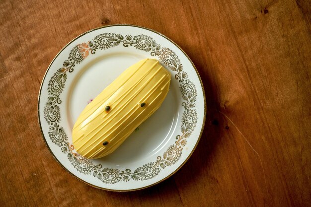 Eclair à la mangue avec glaçage jaune en plaque blanche sur fond de bois