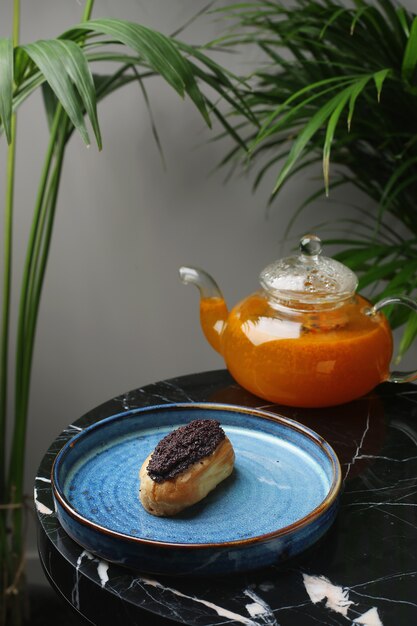 Eclair sur plaque en céramique et tasse de thé sur pierre de marbre et plantes tropicales sur fond.