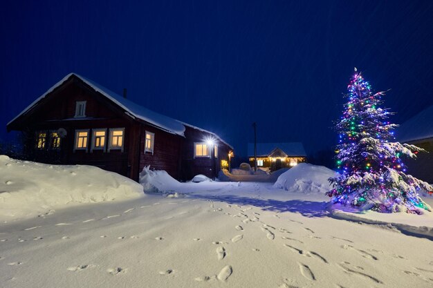 Photo Éclairage électrique dans les fenêtres d'une maison de campagne dans un village de nuit enneigée la veille de noël dans le nord