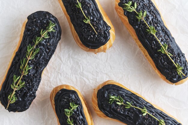 Eclairs à la crème de pistache et glaçage noir. Gâteaux décorés de brins de thym. Dessert sur la table de cuisine blanche.