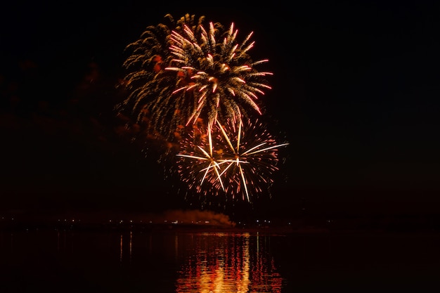 Des éclairs de feux d'artifice festifs au-dessus de la rivière nocturne se reflètent dans l'eau