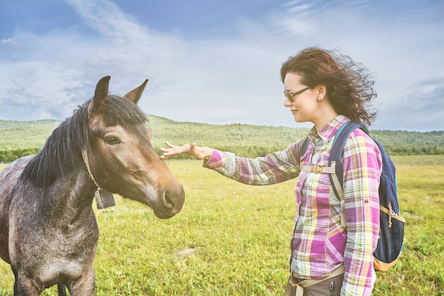 Eco tourisme sur le ranch de fermier, belle femme de race blanche caressant le visage de l'étalon brun dans les pâturages d'été.