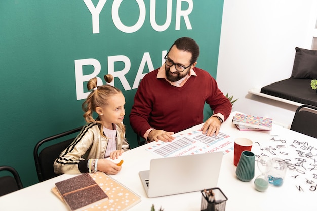 À l'école. Enseignant souriant barbu aux cheveux noirs portant des lunettes expliquant le nouveau matériel à son élève