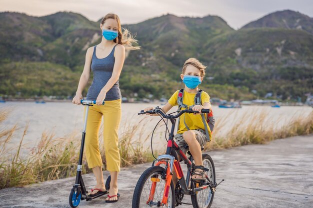 Un écolier actif et sa mère en masque médicale à vélo avec un sac à dos par une journée ensoleillée Un enfant heureux à vélo sur le chemin de l'école Vous devez aller à l'école en masque à cause de l'épidémie de coronavirus