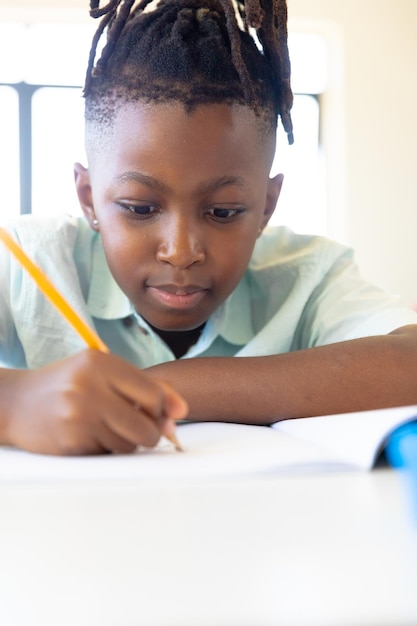 Photo Écolier afro-américain écrivant sur un livre à son bureau en classe.