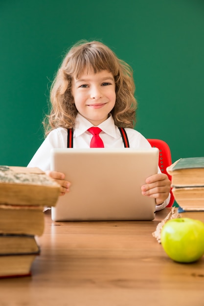 Écolier assis au bureau en classe. Enfant heureux contre le tableau vert. Notion d'éducation
