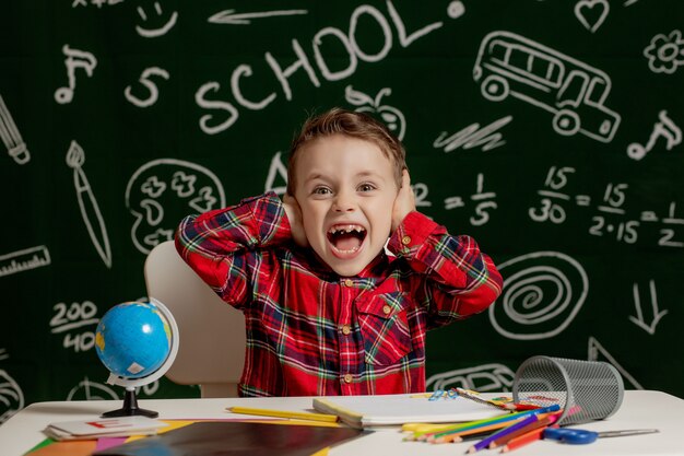 écolier assis au bureau avec de nombreuses fournitures scolaires