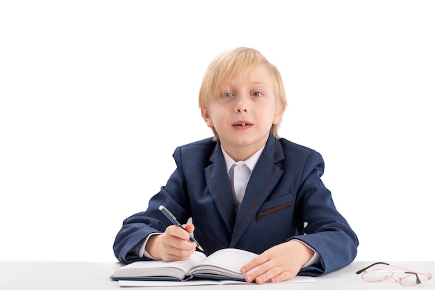 Un écolier blond est assis à un bureau avec un stylo et écoute attentivement l'enseignant Première niveleuse en classe Concept d'éducation