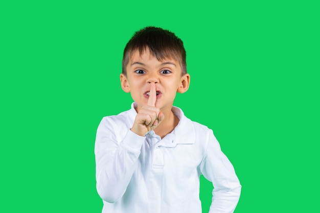 Un écolier en chemise blanche montre tranquillement son index et se penche sur l'appareil photo vert