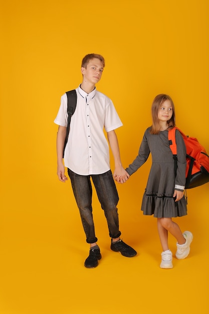 écolier en chemise blanche et pantalon gris tient la main de sa sœur cadette dans un gris d'école