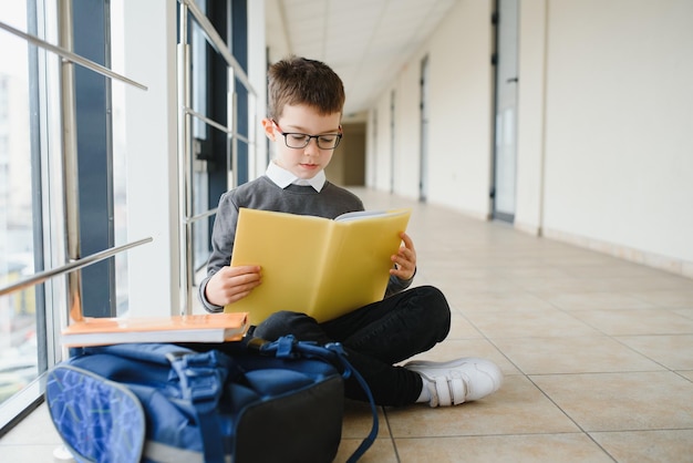 Un écolier est assis sur le sol d'un couloir d'école et lit un livre