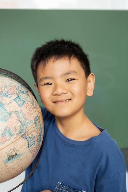 Photo Écolier avec un globe debout contre un tableau vert dans une salle de classe