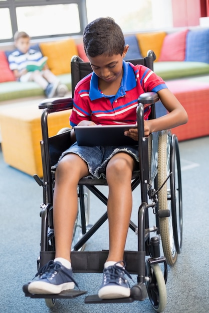 Photo Écolier handicapé en fauteuil roulant à l'aide de tablette numérique dans la bibliothèque