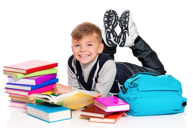 Un écolier heureux allongé sur le sol avec un sac à dos et des livres isolés sur un fond blanc