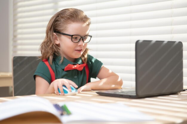 Un écolier intelligent apprenant à distance virtuel en ligne, regardant une leçon de classe numérique à distance, regardant un ordinateur portable étudiant à la maison.