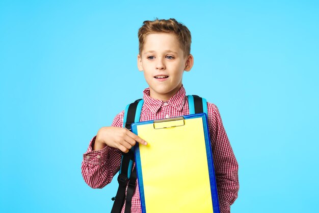 Un écolier joyeux, un sac à dos d'apprentissage, un fond bleu isolé.