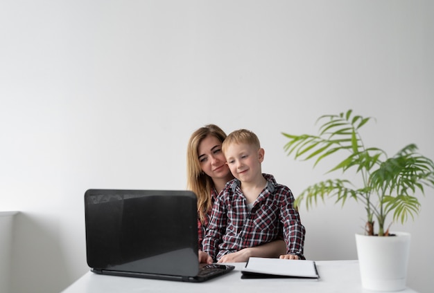 L'écolier et sa mère font leurs devoirs ensemble. Ils sont assis à une table et lisent une tâche sur un ordinateur portable. L'enseignement à distance. Les parents aident les enfants aux écoliers. Cours en ligne.