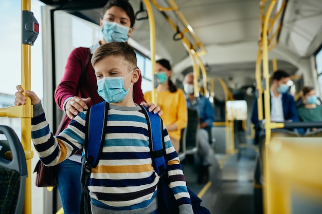 Un écolier et sa mère portant des masques faciaux en montant dans les transports en commun